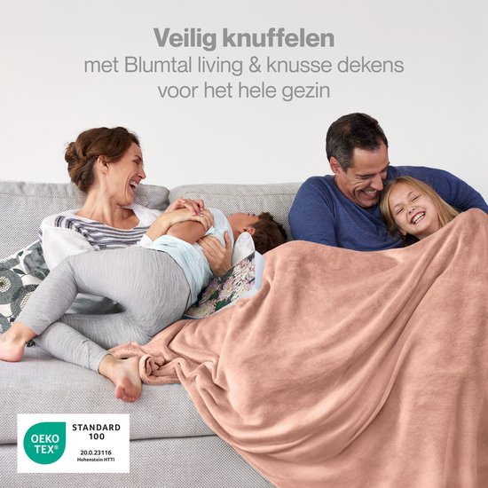 Een gezin knuffelt met een oud roze Blumtal deken op een grijze bank.