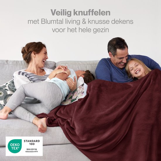 Een gezin lacht samen op een bank onder een grote bordeauxrode deken. Gecertificeerd met OEKO-TEX.