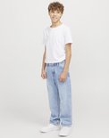 Jongen lacht en draagt een wijde, lichtblauwe spijkerbroek en witte sneakers.