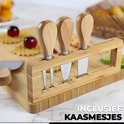 Close-up van houten borrelplank met bamboe mesjeshouder en vier kaasmesjes met houten handvat.