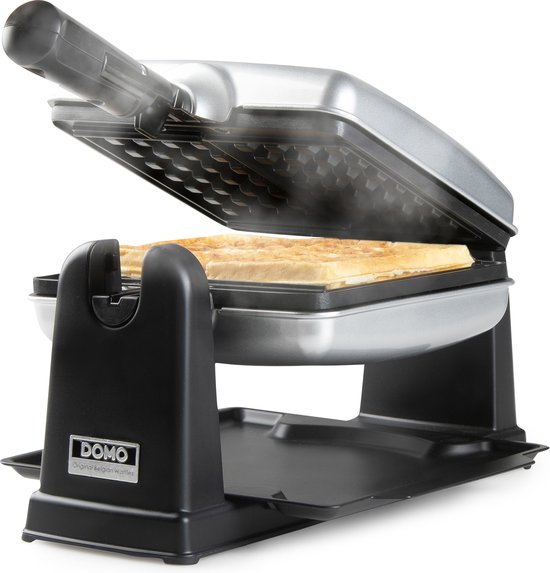 Zilverkleurig wafelijzer bakt wafels, stoom komt van de wafels. Wafels en fruit ernaast.