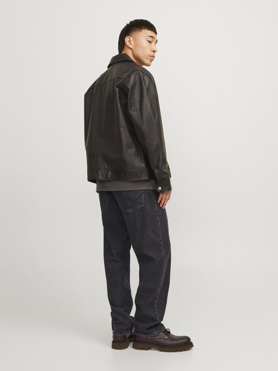 Model draagt losse, zwarte jeans met leren jack.