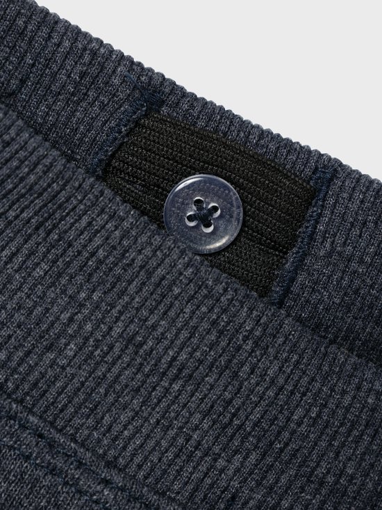 Detail van de tailleband van een donkerblauwe joggingbroek met een knoop.