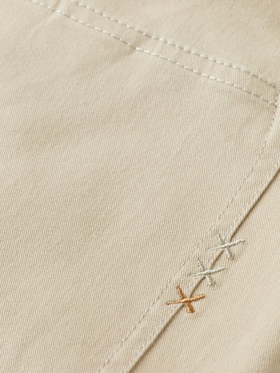 Close-up van beige stof met drie geborduurde kruisjes in verschillende kleuren bij de zak.