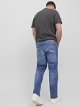 Man van achteren, draagt een grijze t-shirt en blauwe jeans. De jeans is effen van kleur met oranje stiksels.