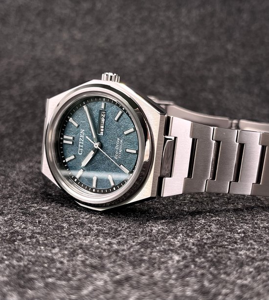 Citizen horloge met blauw-grijze wijzerplaat en titanium band. De wijzerplaat heeft markeringen en datum.