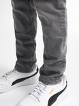 Jongen in grijze jeans met witte Puma sneakers.