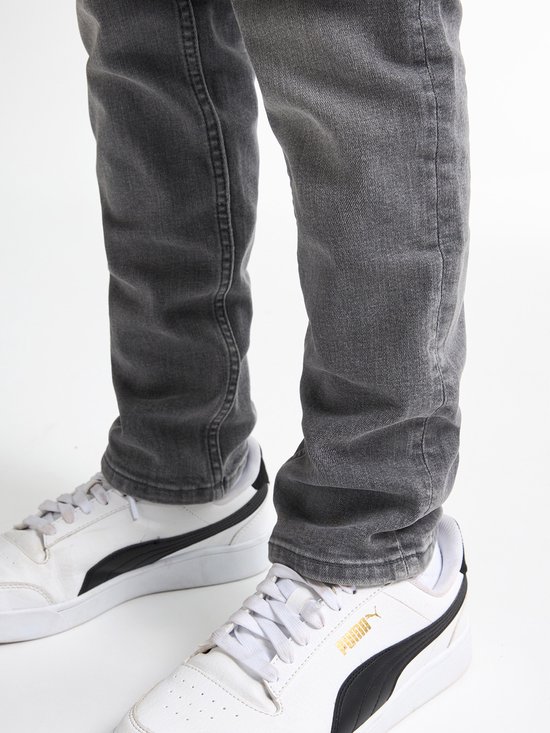 Jongen in grijze jeans met witte Puma sneakers.