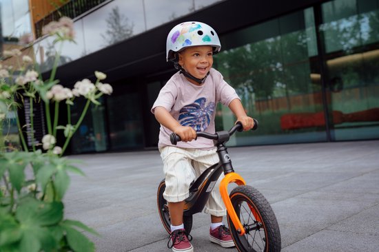 Een jongetje met een witte helm met kleurrijke opdruk, rijdend op een fiets.