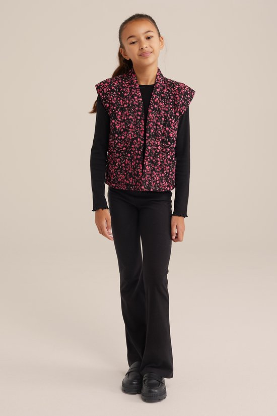 Meisje draagt een zwarte flared legging, een zwart shirt met ruches en een zwart bodywarmer met roze bloemenprint.
