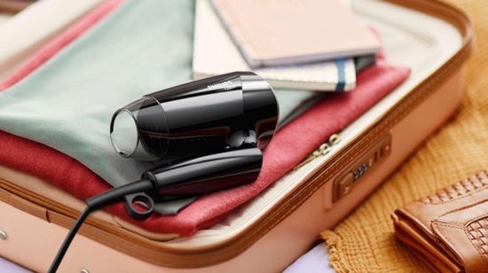 Zwarte compacte Philips föhn in een koffer, tussen kleding en notitieboekjes.