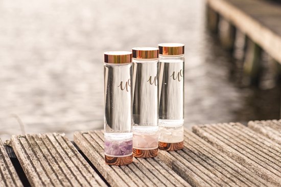 Drie glazen waterflessen met koperkleurige dop en kristallen op houten planken.