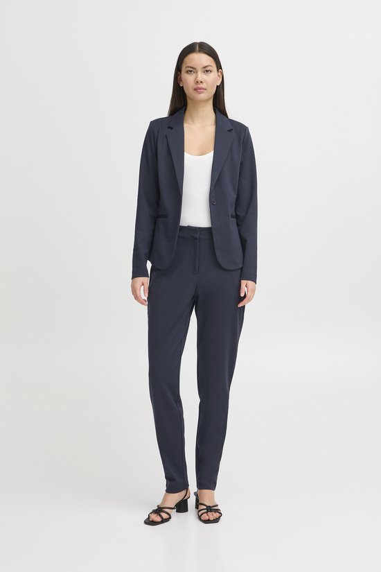 Model in donkerblauwe blazer met bijpassende broek en witte top.