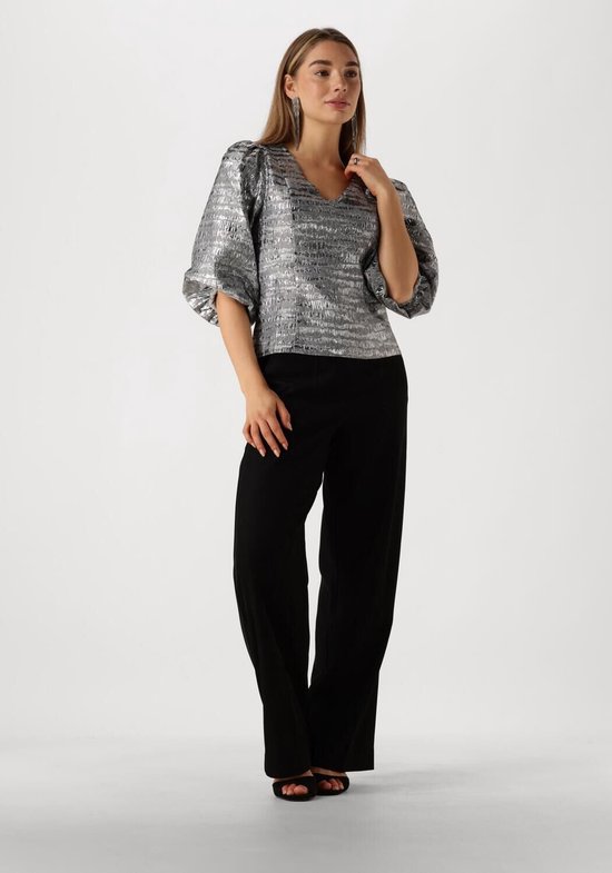 Model draagt zilveren blouse met pofmouwen en V-hals, gecombineerd met zwarte broek.
