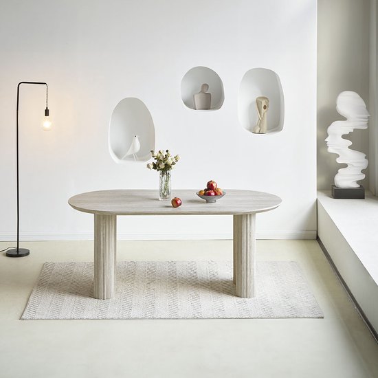 Een ovale, lichtgrijze eettafel met gecanneleerde poten, versierd met een vaas bloemen en een schaal appels.