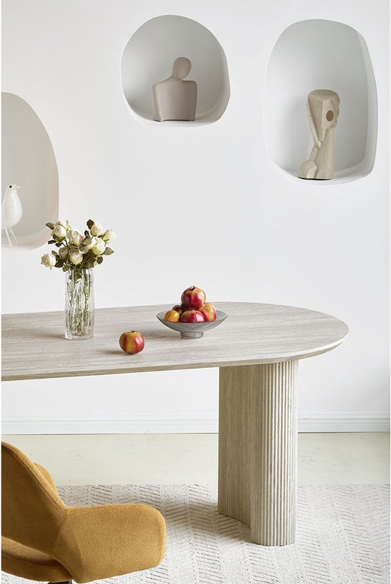 Een zachtgele stoel naast een ovale, lichtgrijze eettafel met gecanneleerde poten op een vloerkleed.