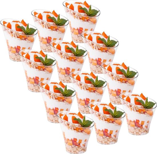 Twaalf transparante plastic dessertbekers gevuld met yoghurt, muesli, stukjes abrikoos en gegarneerd met een muntblaadje.
