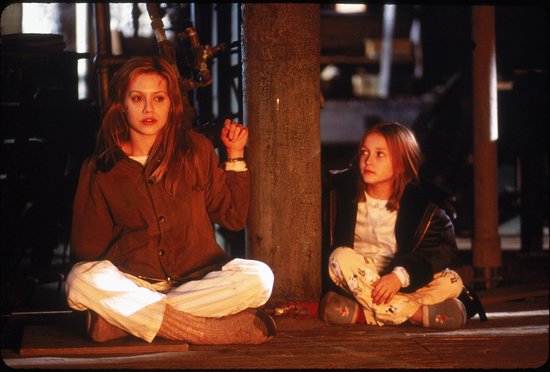 Brittany Murphy en Dakota Fanning zitten op de grond, gekleed in pyjama's en een jas.
