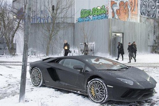 Een zwarte Lamborghini in de sneeuw met mensen op de achtergrond.