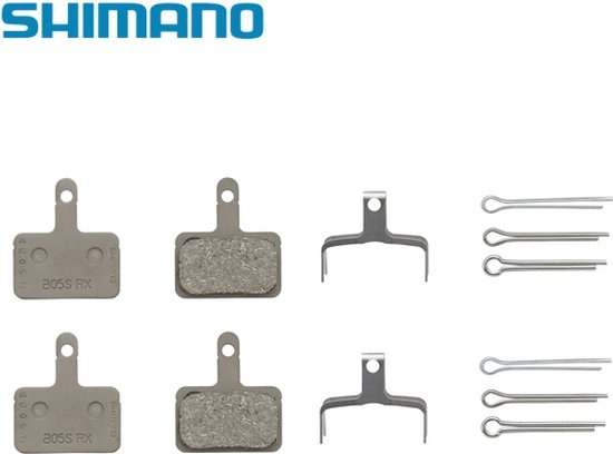 Logo Shimano avec deux plaquettes de frein à surface rugueuse, deux supports métalliques et six goupilles argentées.