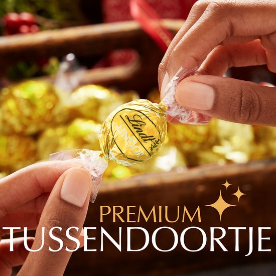 Lindt LINDOR witte chocoladebonbon met goudfolie, vastgehouden tussen twee handen. Premium tussendoortje.