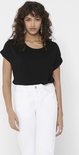 Vrouw draagt een zwarte top met opgerolde korte mouwen en een witte jeans. Ze draagt opvallende oorbellen.