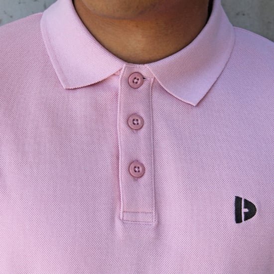 Roze poloshirt met knoopjes en een zwart logo op de borst.