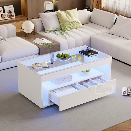 Witte salontafel met glazen blad, blauw LED-licht en open lade met boeken, naast witte hoekbank.