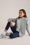 Meisje in donkerblauwe legging, witte t-shirt en grijze hoodie, zittend.