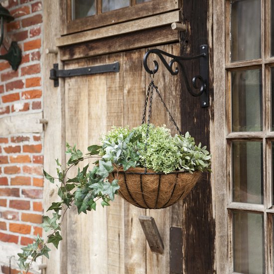 Hangende bloempot met kettingen aan een houten schuur. Gevuld met groene planten en klimop.