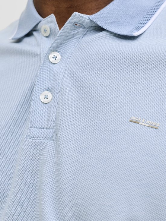Close-up van de kraag en knopen van een lichtblauw poloshirt met logo.