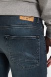Close-up van de achterkant van een donkerblauwe jeans met label 'Crafting Quality Garments'.