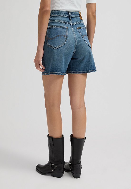 Achterkant van een vrouw in een spijkerbroek met wijde pijpen en zwarte cowboylaarzen.