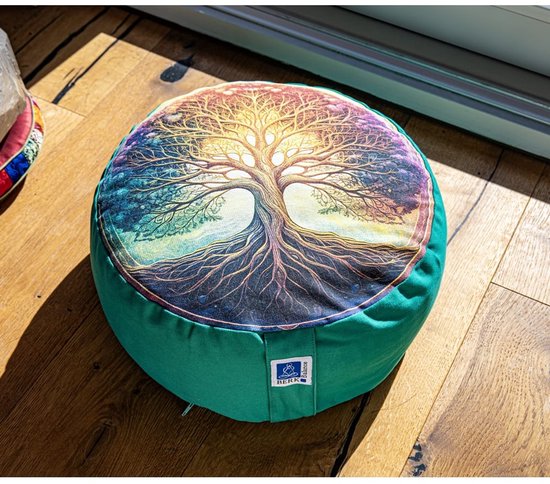 Groen meditatiekussen met de Levensboom print, op een houten vloer. De boom heeft een oranje zon als achtergrond.
