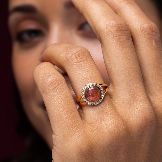Gouden ring met ronde, roze steen en zirkonia steentjes op de hand van een model.