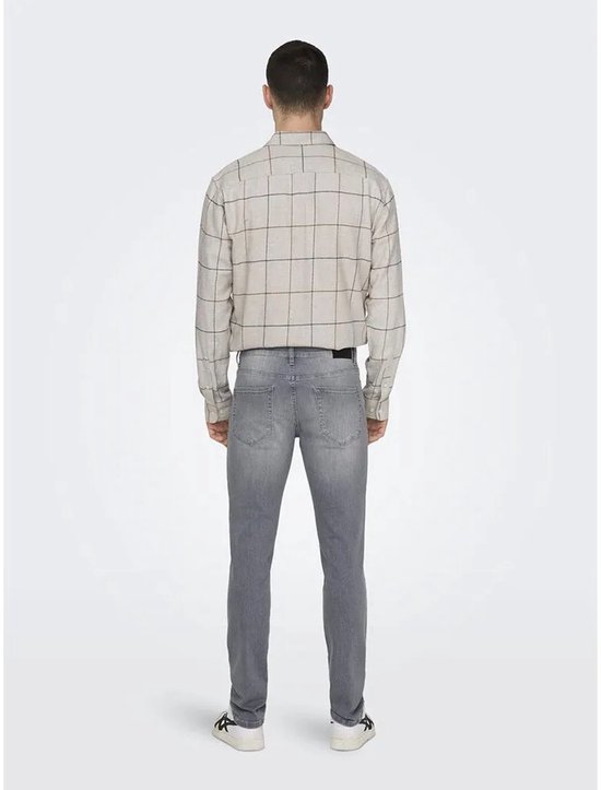 Man in grijze jeans en een beige geruit overhemd, gezien vanaf de achterkant.