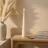 Crèmekleurige kegelvormige LED-kaars op een houten kastje met een vaas met pluimen en boeken.