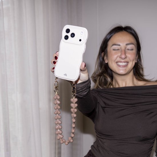 Vrolijke vrouw met gesloten ogen toont een off-white golvend telefoonhoesje met bruin hartjeskoord.