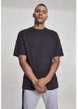 Man staat frontaal in zwart oversized T-shirt en grijze joggingbroek met zwarte streep, handen gevouwen.