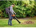 Man gebruikt oranje bladblazer met opvangzak om bladeren op te zuigen in de tuin.