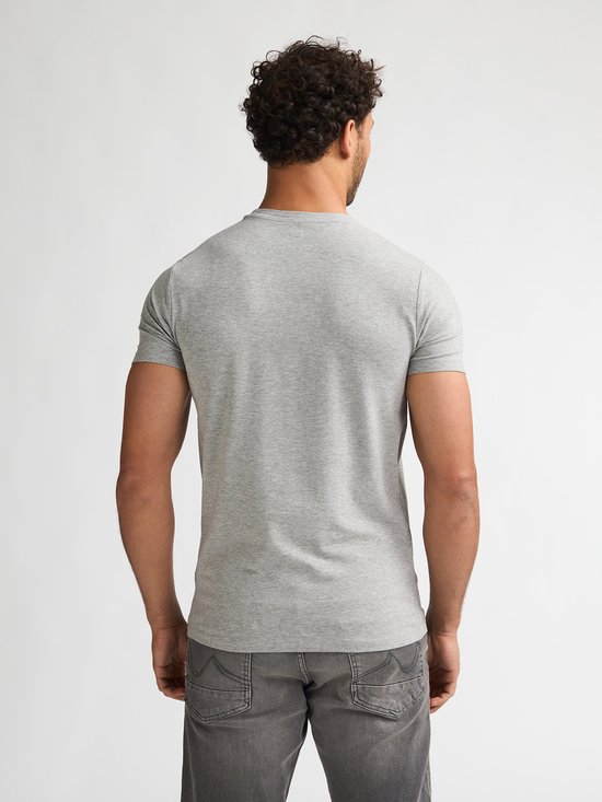 Man met krullend haar, achterkant van een effen lichtgrijs T-shirt met ronde hals.
