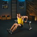 Man met gele tanktop doet dips op een zwarte trainingsbank.