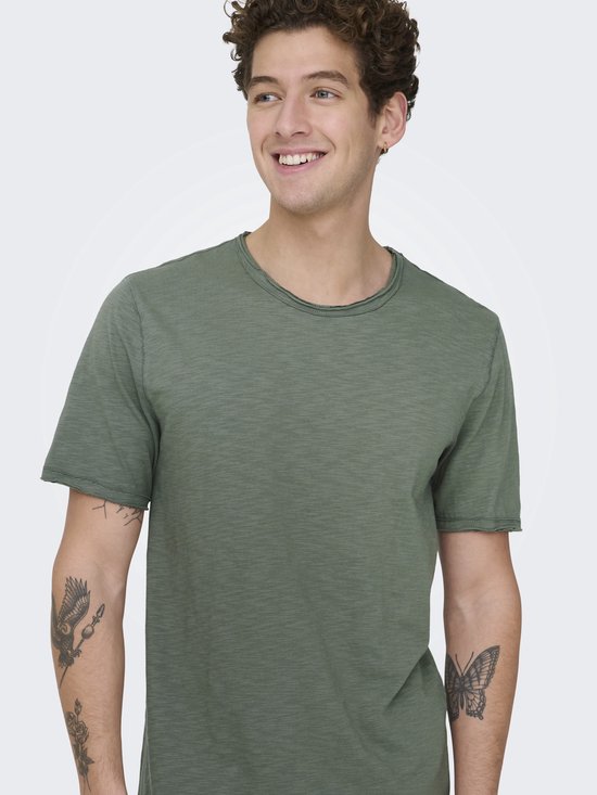 Man met tatoeages op zijn armen, glimlachend in een olijfgroen T-shirt.