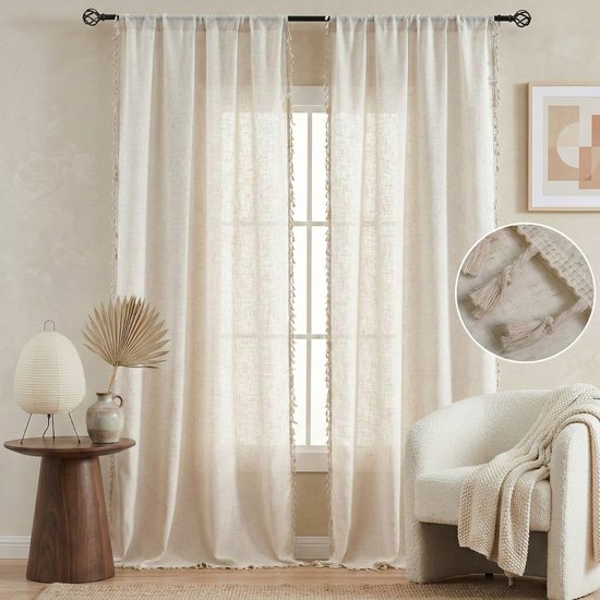 Twee crème vitrages met decoratieve beige kwastjes, hangend voor een raam.