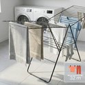 Porte-linge noir avec serviettes grises et beiges, chemisier blanc et bleu, chaussettes et indication de 32m de longueur de séchage.