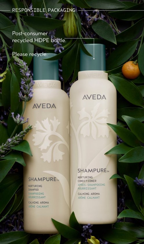 Twee Aveda Shampure flessen, één shampoo en één conditioner, omringd door groene bladeren en lavendel.