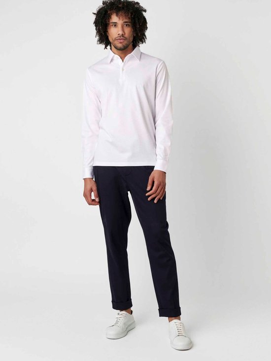Man in wit longsleeve poloshirt en donkerblauwe broek, staand.