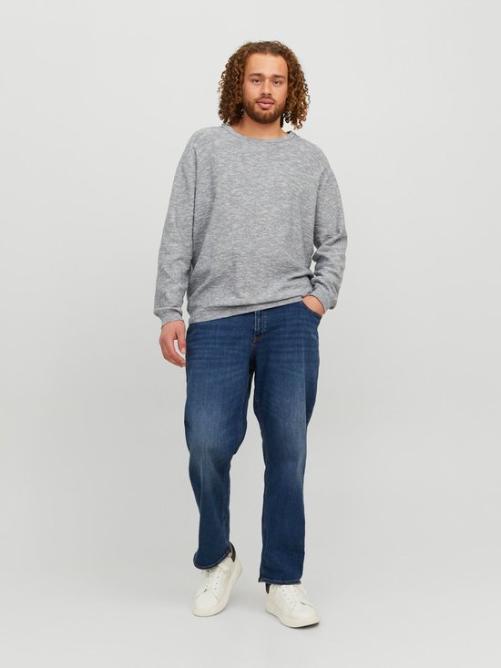 Man met krullend haar draagt een lichtgrijs gemêleerde sweater en een spijkerbroek van blauw denim.