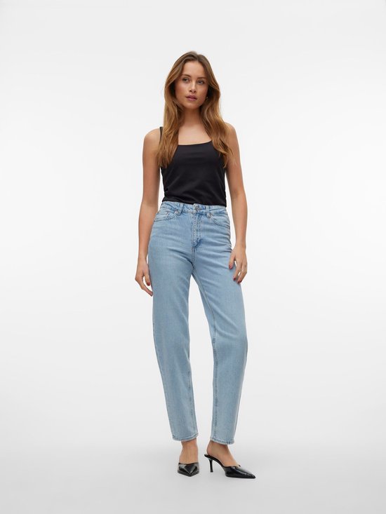 Model in lichtblauwe mom fit jeans met hoge taille, zwart topje en zwarte hakken.