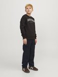 Jongens in een zwarte trui met logo en donkere cargobroek, met bruine sneakers met witte strepen.